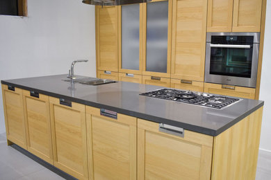 Example of a minimalist single-wall kitchen design in New York with an undermount sink, light wood cabinets, stainless steel appliances, an island and gray countertops