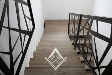 Réalisation d'un grand escalier design en U avec des marches en bois et un garde-corps en métal.