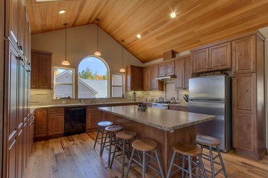 Photo of a mid-sized traditional u-shaped kitchen in Sacramento with an undermount sink, raised-panel cabinets, medium wood cabinets, granite benchtops, stainless steel appliances, light hardwood floors, with island and brown floor.