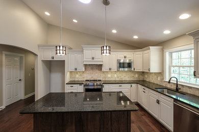 Large transitional l-shaped dark wood floor and brown floor eat-in kitchen photo in Other with an undermount sink, raised-panel cabinets, white cabinets, granite countertops, beige backsplash, ceramic backsplash, stainless steel appliances, an island and brown countertops