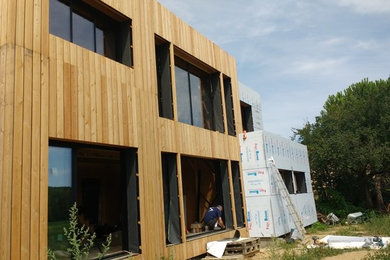 Cette image montre une façade de maison beige design en bois à un étage avec un toit plat.