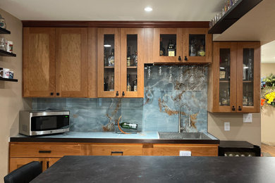 Inspiration for a small transitional galley brown floor wet bar remodel in Denver with a drop-in sink, shaker cabinets, medium tone wood cabinets, laminate countertops, blue backsplash and black countertops