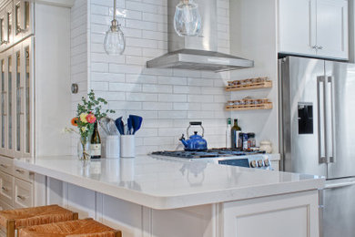 Inspiration for a small coastal l-shaped light wood floor and beige floor open concept kitchen remodel in Other with a farmhouse sink, recessed-panel cabinets, white cabinets, quartz countertops, white backsplash, subway tile backsplash, stainless steel appliances, a peninsula and white countertops