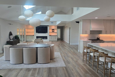 Example of a mid-sized minimalist open concept vinyl floor, gray floor and exposed beam living room design in Orange County with white walls, a standard fireplace, a plaster fireplace and a wall-mounted tv