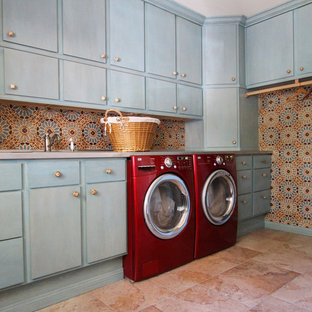 Imagen de cuarto de lavado en L, mediterráneo, grande, con armarios con paneles lisos, puertas de armario azules, lavadora y secadora juntas, suelo rosa, suelo de piedra caliza y paredes multicolor