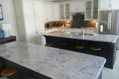 Example of a mid-sized beach style l-shaped porcelain tile and white floor eat-in kitchen design in Jacksonville with a double-bowl sink, recessed-panel cabinets, beige cabinets, granite countertops, black backsplash, glass tile backsplash, stainless steel appliances and two islands