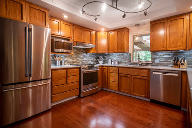 Example of a large classic u-shaped vinyl floor and brown floor kitchen design in Other with a double-bowl sink, medium tone wood cabinets, quartzite countertops, gray backsplash, glass tile backsplash, stainless steel appliances and white countertops