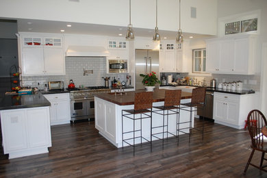 Inspiration for a large timeless u-shaped dark wood floor and brown floor eat-in kitchen remodel in San Francisco with a farmhouse sink, recessed-panel cabinets, white cabinets, gray backsplash, subway tile backsplash, stainless steel appliances and an island
