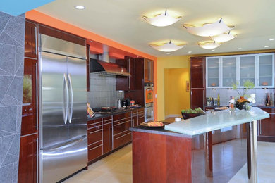 Large trendy ceramic tile and beige floor kitchen photo in San Francisco with flat-panel cabinets, brown cabinets, glass countertops, metallic backsplash, cement tile backsplash, stainless steel appliances and an island