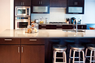 Inspiration for a contemporary u-shaped enclosed kitchen remodel in Philadelphia with an undermount sink, flat-panel cabinets, dark wood cabinets, quartz countertops, gray backsplash, glass tile backsplash, stainless steel appliances and an island
