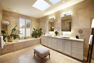 This is an example of a mid-sized contemporary master bathroom in Brisbane with open cabinets, a corner tub, beige tile, limestone, beige walls, marble floors, limestone benchtops and beige floor.