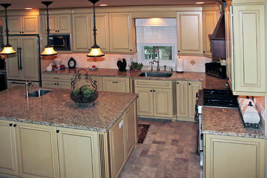Inspiration for a large timeless u-shaped ceramic tile eat-in kitchen remodel in New York with an undermount sink, raised-panel cabinets, yellow cabinets, granite countertops, beige backsplash, stone tile backsplash, stainless steel appliances and an island