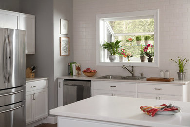 Example of a mid-sized trendy l-shaped dark wood floor and brown floor open concept kitchen design in Philadelphia with a drop-in sink, recessed-panel cabinets, white cabinets, quartz countertops, white backsplash, subway tile backsplash, stainless steel appliances and an island