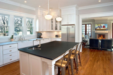 Elegant l-shaped medium tone wood floor enclosed kitchen photo in Atlanta with a farmhouse sink, shaker cabinets, white cabinets, white backsplash, subway tile backsplash, stainless steel appliances and an island