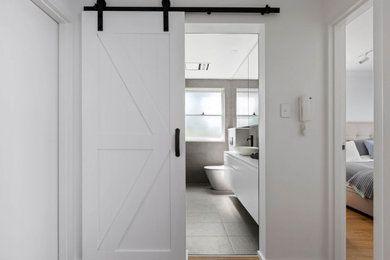 This is an example of a mid-sized contemporary 3/4 bathroom in Sydney with flat-panel cabinets, white cabinets, an alcove shower, a wall-mount toilet, gray tile, ceramic tile, grey walls, cement tiles, a vessel sink, engineered quartz benchtops, grey floor, a hinged shower door, grey benchtops, an enclosed toilet, a single vanity and a built-in vanity.