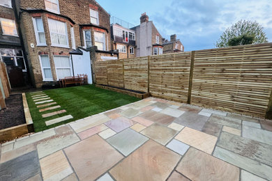 Medium sized modern back formal partial sun garden fence for spring in London with natural stone paving and a wood fence.