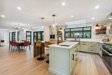 Mid-sized cottage l-shaped light wood floor and beige floor eat-in kitchen photo in DC Metro with an island, a farmhouse sink, raised-panel cabinets, green cabinets, quartz countertops, gray backsplash, porcelain backsplash, stainless steel appliances and white countertops