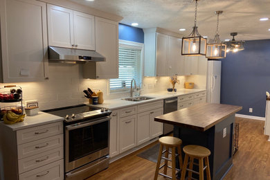 Example of a mid-sized transitional galley laminate floor and brown floor eat-in kitchen design in Louisville with an undermount sink, shaker cabinets, white cabinets, quartz countertops, white backsplash, ceramic backsplash, stainless steel appliances, an island and white countertops