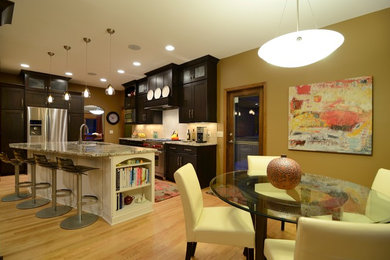 Transitional light wood floor open concept kitchen photo in Minneapolis with a double-bowl sink, flat-panel cabinets, dark wood cabinets, granite countertops, white backsplash, limestone backsplash, stainless steel appliances and an island