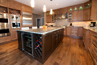 This is an example of a large contemporary galley eat-in kitchen in Edmonton with an undermount sink, recessed-panel cabinets, medium wood cabinets, granite benchtops, stainless steel appliances, medium hardwood floors and with island.