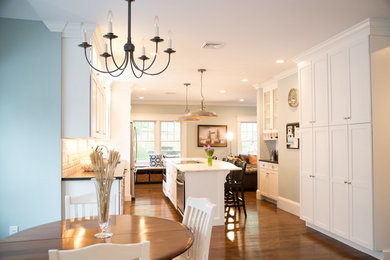 Example of a mid-sized country galley medium tone wood floor and brown floor enclosed kitchen design in Boston with an undermount sink, shaker cabinets, white cabinets, stainless steel appliances, an island, solid surface countertops, white backsplash and subway tile backsplash