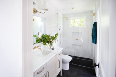 サンフランシスコにある高級な中くらいなトランジショナルスタイルのおしゃれな浴室 (置き型浴槽、白いタイル、白い壁、黒い床、開き戸のシャワー、洗面台1つ、造り付け洗面台、一体型トイレ	、セラミックタイル、白い洗面カウンター、落し込みパネル扉のキャビネット) の写真