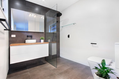 Design ideas for a large modern 3/4 bathroom in Wollongong with flat-panel cabinets, white cabinets, an open shower, a one-piece toilet, multi-coloured tile, ceramic tile, multi-coloured walls, ceramic floors, a vessel sink, wood benchtops, grey floor, an open shower and brown benchtops.