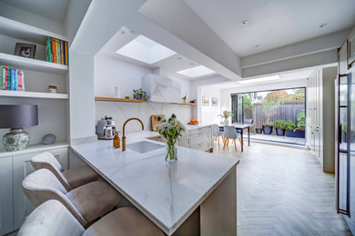 Design ideas for a contemporary l-shaped open plan kitchen in London with a submerged sink, shaker cabinets, beige cabinets, quartz worktops, multi-coloured splashback, engineered quartz splashback, integrated appliances, light hardwood flooring, a breakfast bar, brown floors, multicoloured worktops and a drop ceiling.