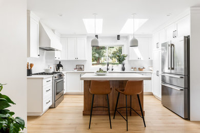 Mid-sized country u-shaped vinyl floor and beige floor open concept kitchen photo in Vancouver with an undermount sink, shaker cabinets, white cabinets, quartz countertops, white backsplash, ceramic backsplash, stainless steel appliances, an island and white countertops