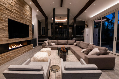 Inspiration for a large contemporary open concept living room in Denver with a home bar, grey walls, medium hardwood floors, a standard fireplace, a stone fireplace surround, a wall-mounted tv and grey floor.