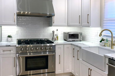 Inspiration for a mid-sized transitional l-shaped light wood floor and brown floor eat-in kitchen remodel in New York with a farmhouse sink, shaker cabinets, white cabinets, quartz countertops, white backsplash, ceramic backsplash, stainless steel appliances, an island and white countertops