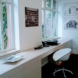 Medium sized modern study in Frankfurt with white walls, carpet, a built-in desk and black floors.