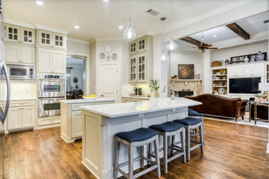 Eat-in kitchen - mid-sized country u-shaped light wood floor and brown floor eat-in kitchen idea in Dallas with a farmhouse sink, shaker cabinets, beige cabinets, quartz countertops, white backsplash, ceramic backsplash, stainless steel appliances, an island and white countertops