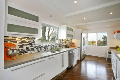 This is an example of a mid-sized contemporary galley separate kitchen in Orange County with a double-bowl sink, flat-panel cabinets, white cabinets, quartz benchtops, multi-coloured splashback, matchstick tile splashback, stainless steel appliances, medium hardwood floors and no island.