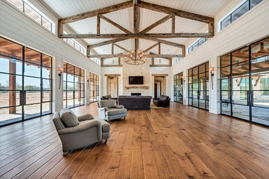 This is an example of a country open concept living room in Dallas with medium hardwood floors, a standard fireplace, a stone fireplace surround, a wall-mounted tv and brown floor.