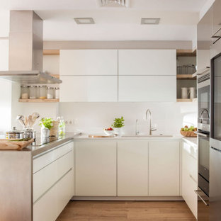Foto de cocina en U, actual, con fregadero bajoencimera, armarios con paneles lisos, puertas de armario blancas, electrodomésticos de acero inoxidable, suelo de madera clara, península, suelo beige y encimeras grises