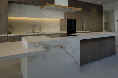 Photo of a modern galley open plan kitchen in Melbourne with an undermount sink, flat-panel cabinets, medium wood cabinets, tile benchtops, white splashback, ceramic splashback, black appliances, ceramic floors, with island, beige floor and white benchtop.