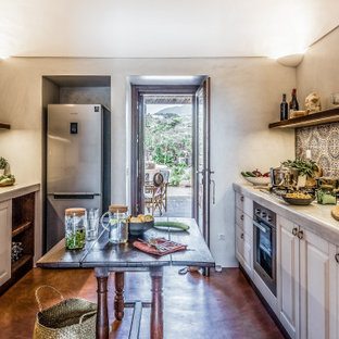 Immagine di una cucina parallela mediterranea chiusa con lavello sottopiano, ante con bugna sagomata, ante bianche, paraspruzzi multicolore, elettrodomestici in acciaio inossidabile, pavimento in cemento, 2 o più isole, pavimento marrone e top grigio