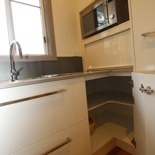 Photo of a small contemporary u-shaped kitchen pantry in Sydney with a double-bowl sink, flat-panel cabinets, beige cabinets, quartz benchtops, metallic splashback, glass sheet splashback, stainless steel appliances, light hardwood floors and no island.
