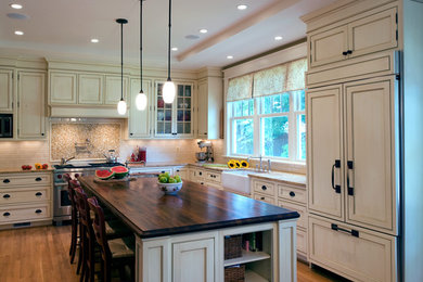 Kitchen - large traditional l-shaped medium tone wood floor and brown floor kitchen idea in Baltimore with a farmhouse sink, recessed-panel cabinets, beige cabinets, beige backsplash, subway tile backsplash, stainless steel appliances, an island and beige countertops