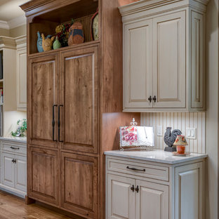 Exemple d'une très grande arrière-cuisine nature en L avec un évier de ferme, un placard avec porte à panneau surélevé, des portes de placard beiges, un plan de travail en granite, une crédence beige, une crédence en carreau de céramique, un électroménager encastrable, un sol en bois brun, un îlot central, un sol marron et un plan de travail beige.