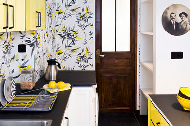 This is an example of an eclectic galley kitchen in Rennes with a drop-in sink, flat-panel cabinets, yellow cabinets, black floor and black benchtop.