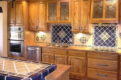 Example of a mid-sized classic single-wall brick floor and red floor open concept kitchen design in Albuquerque with a drop-in sink, raised-panel cabinets, medium tone wood cabinets, blue backsplash, ceramic backsplash, stainless steel appliances and an island