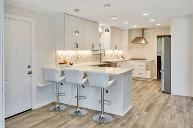 Example of a mid-sized trendy l-shaped porcelain tile and brown floor eat-in kitchen design in Other with a farmhouse sink, shaker cabinets, white cabinets, quartz countertops, beige backsplash, glass sheet backsplash, stainless steel appliances and no island