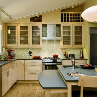 Inredning av ett modernt avskilt l-kök, med stänkskydd i mosaik, rostfria vitvaror, en undermonterad diskho, luckor med glaspanel, skåp i ljust trä och grönt stänkskydd