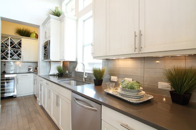 Mid-sized transitional l-shaped light wood floor and brown floor enclosed kitchen photo in Denver with an undermount sink, shaker cabinets, white cabinets, quartz countertops, beige backsplash, glass tile backsplash and stainless steel appliances