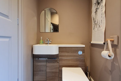 Photo of a small contemporary cloakroom in Other with flat-panel cabinets, medium wood cabinets, a one-piece toilet, brown walls, vinyl flooring, a built-in sink, solid surface worktops, white worktops and a built in vanity unit.