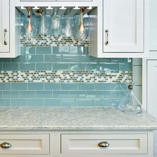 На фото: угловая кухня среднего размера с кладовкой, раковиной в стиле кантри, фасадами с утопленной филенкой, желтыми фасадами, столешницей из кварцевого композита, синим фартуком, фартуком из керамической плитки и техникой из нержавеющей стали без острова с