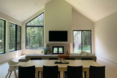 Modelo de salón minimalista con paredes blancas, suelo de madera clara, chimenea de doble cara y televisor colgado en la pared