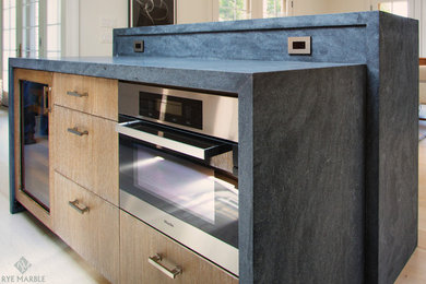 Example of a mid-sized trendy light wood floor eat-in kitchen design in New York with an undermount sink, flat-panel cabinets, light wood cabinets, limestone countertops, gray backsplash, stone slab backsplash, stainless steel appliances and an island